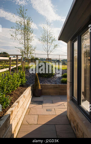 Side of a house - beautiful, landscaped, private garden (modern design, paved path, shrubs on raised border with slate). Yorkshire, England, UK. Stock Photo