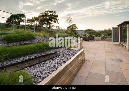 Beautiful, landscaped, private garden with contemporary design, paved patio, shrubs & grasses in lines on raised border - Yorkshire, England, UK. Stock Photo