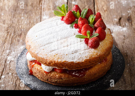 Home Victoria sponge cake, decorated with strawberries, cranberries and mint closeup on the table. Horizontal Stock Photo