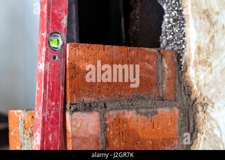 Close up of bricklaying industrial installing bricks on construction site wall with working tools, mortar, level Stock Photo