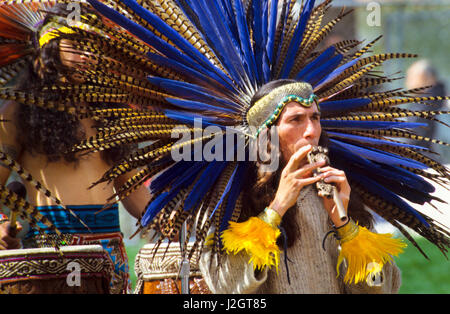 Aztec man dressed in traditional headdress and snake headband plays a traditional wooden whistle flute during a musical presentation in Malibu Beach, CA Stock Photo