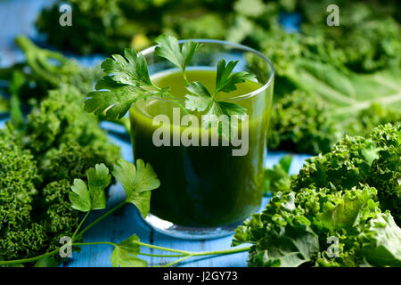 a glass with kale smoothie topped with a twig of parsley and some leaves of kale on a blue rustic wooden table Stock Photo