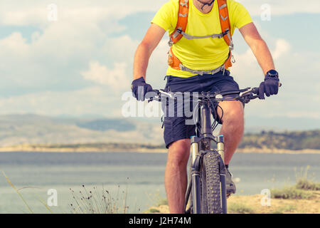 Mountain biker riding on bike at the sea and summer mountains. Man rider cycling MTB on country road or single track. Sport fitness motivation, inspir Stock Photo
