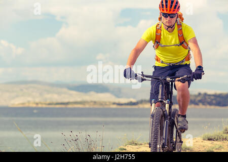 Mountain biker riding on bike at the sea and summer mountains. Man rider cycling MTB on country road or single track. Sport fitness motivation, inspir Stock Photo