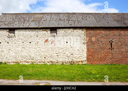 an old rustic barn made from white stone and orange brick with windows and wooden shutters on a grassy bank Stock Photo