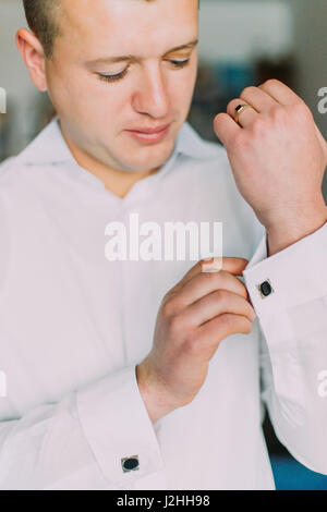 Young man in white shirt fixing his cufflinks while cressing. Close-up. Stock Photo