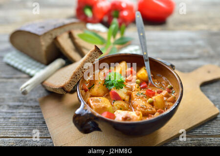 Hot vegetarian potato goulash served in a ceramic bowl with delicious dark baked farmhouse bread on an old wooden table, a Tyrolean mountain specialty Stock Photo