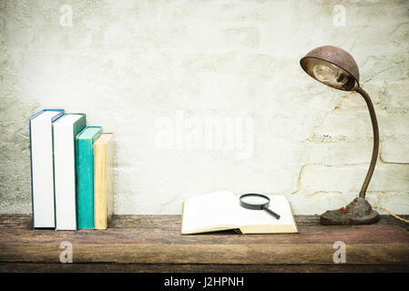 Closeup of workplace with open book stationery items and retro lamp on wooden table with white concrete background. Vintage filtered. Education concep Stock Photo
