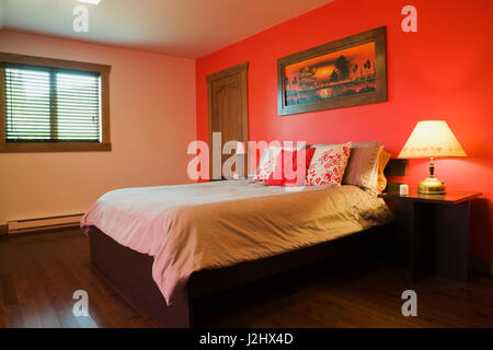 Queen size bed on wooden frame and night tables in bright red painted master bedroom inside a Scandinavian cottage style log home Stock Photo