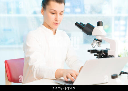 Female scientist using laptop with microscope. Stock Photo