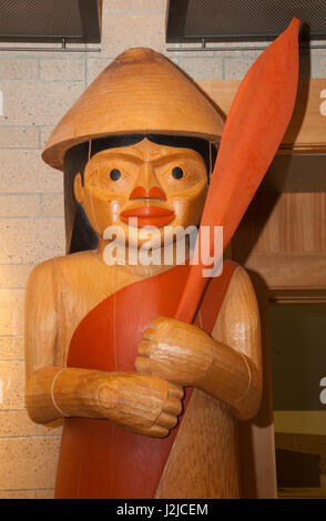 Large cedar wood totem pole carving of a Coast Salish man gathering wearing a conical hat and holds a paddle on display at the Hilbub Cultural Center and Museum located on the Tulalip Tribes Reservation in Marysville, WA Stock Photo