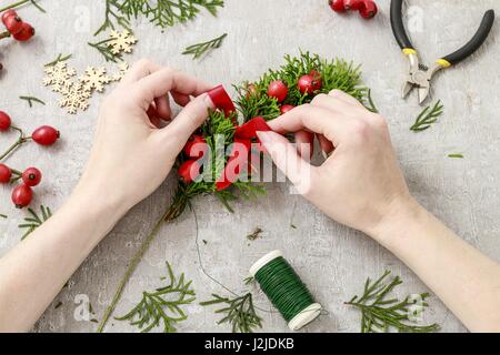 Florist at work: How to make traditional christmas door wreath with thuja twigs and wild rose fruits. Step by step, tutorial. Stock Photo