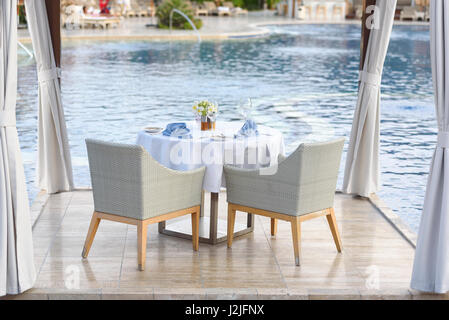 Dinner table for couple with white tablecloth and blue napkins by the pool. Romantic dinner by the pool. Dining table for couple Stock Photo
