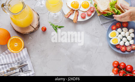 Breakfast table with fried eggs, bacon, cherry tomatoes, sanwiches, orange juice