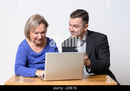 Cheerful cute senior woman in blue shirt using computer beside smiling businessman using laptop computer Stock Photo