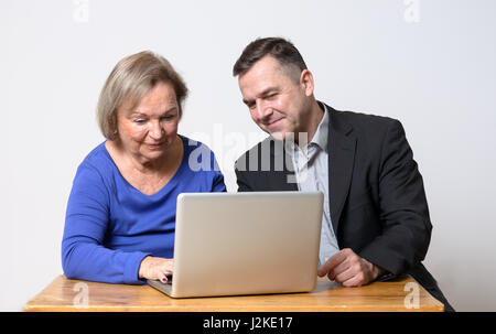 Cheerful cute senior woman in blue shirt using computer beside smiling businessman using laptop computer Stock Photo