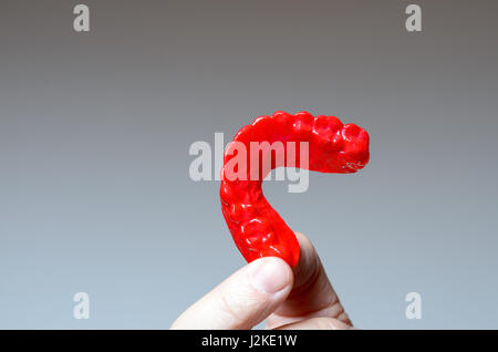 Finger holding a red bite plate to protect his teeth at night from grinding caused by bruxism Stock Photo
