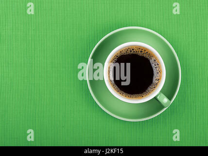 Full cup of black Americano or instant coffee on saucer over green tablecloth, close up, elevated top view Stock Photo