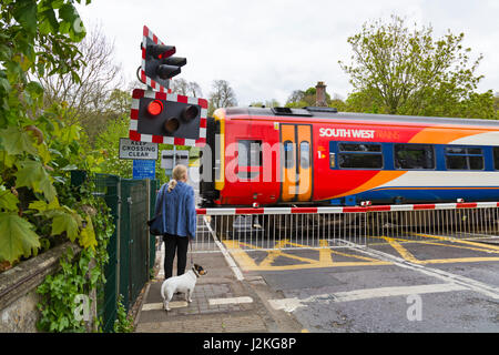 Woman and dog waiting at level crossing barrier for South West Trains train to pass at Sherborne, Dorset, England UK in April Stock Photo