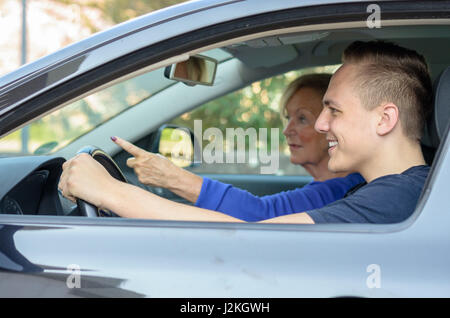 Happy young man giving his grandmother a lift grinning as he drives along while she points at something ahead of them, view through the open window Stock Photo