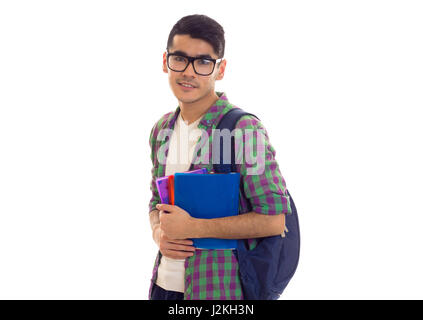 Young smiling man with black hair in white T-shirt and checkered shirt with blue backpack holding books on white background in studio Stock Photo