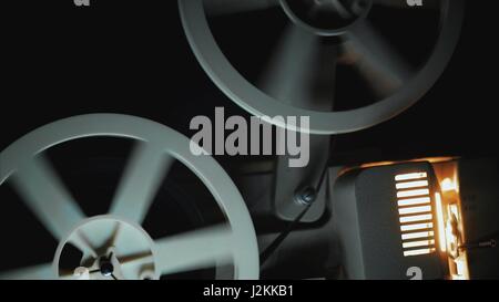 Mechanism of film projector, Front view of an old-fashioned antique Super 8mm film projector, projecting a beam of light in a dark room next to a stac Stock Photo