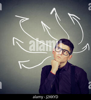 Confused, young business man with many twisted arrows on the concrete wall background Stock Photo