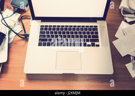 notebook or laptop computer on messy wooden desk, for busy working concept, in vintage retro color style Stock Photo