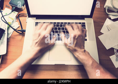blurred male hands typing, working on computer keyboard on busy wooden desk, with vintage color tone Stock Photo