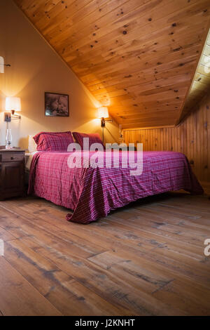 King size bed in master bedroom on the upstairs floor inside a cottage style log home Stock Photo