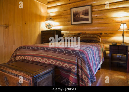 Queen size bed with Navajo patterned bedspread in master bedroom on the ground floor inside a Scandinavian cottage style log home. Stock Photo