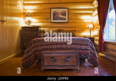 Queen size bed with Navajo patterned bedspread in master bedroom on the ground floor inside a Scandinavian cottage style log home. Stock Photo