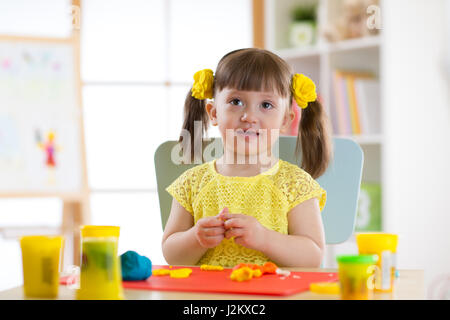 Little girl is learning to use colorful plasticine in well lit room near window Stock Photo