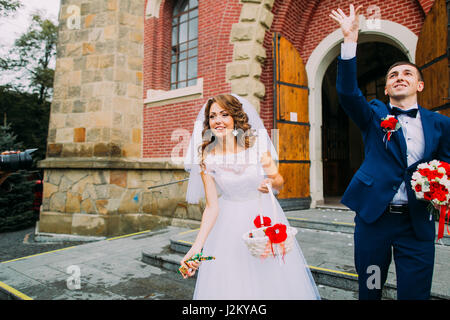 Joyful bride and groom leaving the church after a wedding ceremony Stock Photo