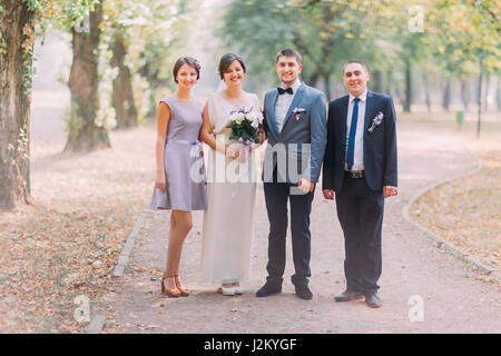 Newlyweds with groomsman and bridesmaid posing at sunny park lane Stock Photo