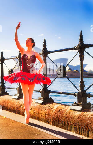 Young fit ballerina in red concert tutu excercising and practicing on street near Sydney harbour The Rocks and Circular quay in warm morning light. Stock Photo