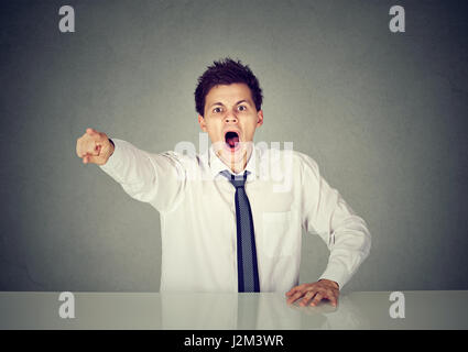 Angry young business man sitting at his desk and screaming Stock Photo
