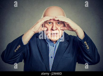 Annoyed elderly man looking through hands like binoculars has vision problems Stock Photo