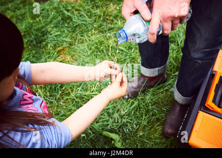 Young girl washing muddy fingers at British allotment with water bottle. Stock Photo