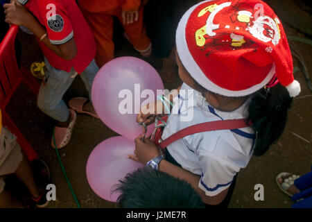 A young girl is wearing a Santa Ckaus hat while holding balloons at a Christmas party at a foreign language school in Tboung Khmum Province,Cambodia. Stock Photo