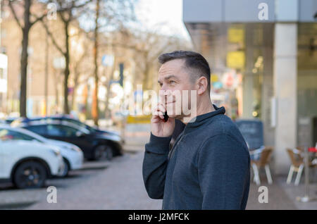 Half body portrait of middle aged man using mobile in city street Stock Photo
