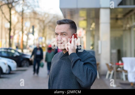 Half body portrait of middle aged man using mobile in city street Stock Photo