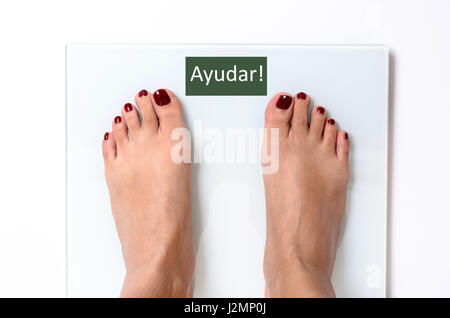 Close-up of incognito woman feet with red nail polish standing on white weight scales with word Ayudar on screen Stock Photo