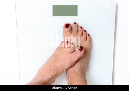 Incognito woman with red pedicure standing with one foot on another on white weight scale with empty green screen Stock Photo