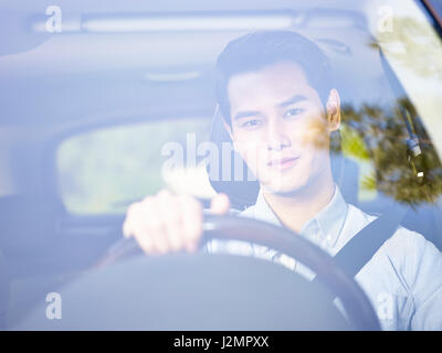 young asian man driving a vehicle seen through the windshield glass. Stock Photo