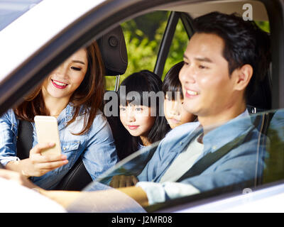happy asian family with two children traveling by car, mother using cellphone while father driving, focus on the little girl. Stock Photo