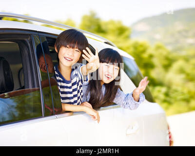 happy asian children sticking heads out of rear window of a car and waving hands. Stock Photo