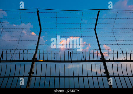 Barbed wire fence silhouettes against cloudy dark blue sky at sunset Stock Photo