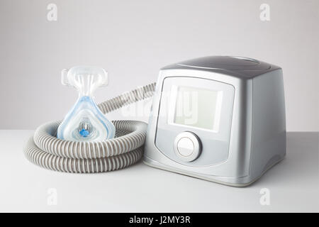 Sleep Apnea CPAP machine with hose and head hear mask, on white table Stock Photo