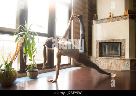 Young attractive woman practicing yoga, stretching in Side Plank exercise, Full Version of Vasisthasana pose, working out, wearing sportswear, pants,  Stock Photo